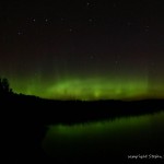 Grüner Polarlichtbogen über einem See in Finnland mit Refelxion