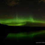 Grüner Polarlichtbogen über einem See in Finnland